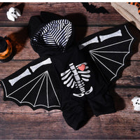 Thumbnail for A black Halloween costume hoodie styled as a bat, featuring white printed bat wings, a white skeleton graphic on the front with a small red heart, and a black-and-white striped hood lining, displayed on a rustic wooden surface with Halloween props.