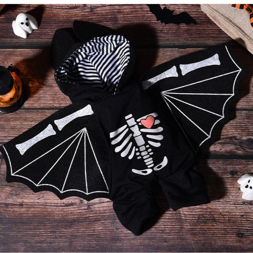 A black Halloween costume hoodie styled as a bat, featuring white printed bat wings, a white skeleton graphic on the front with a small red heart, and a black-and-white striped hood lining, displayed on a rustic wooden surface with Halloween props.